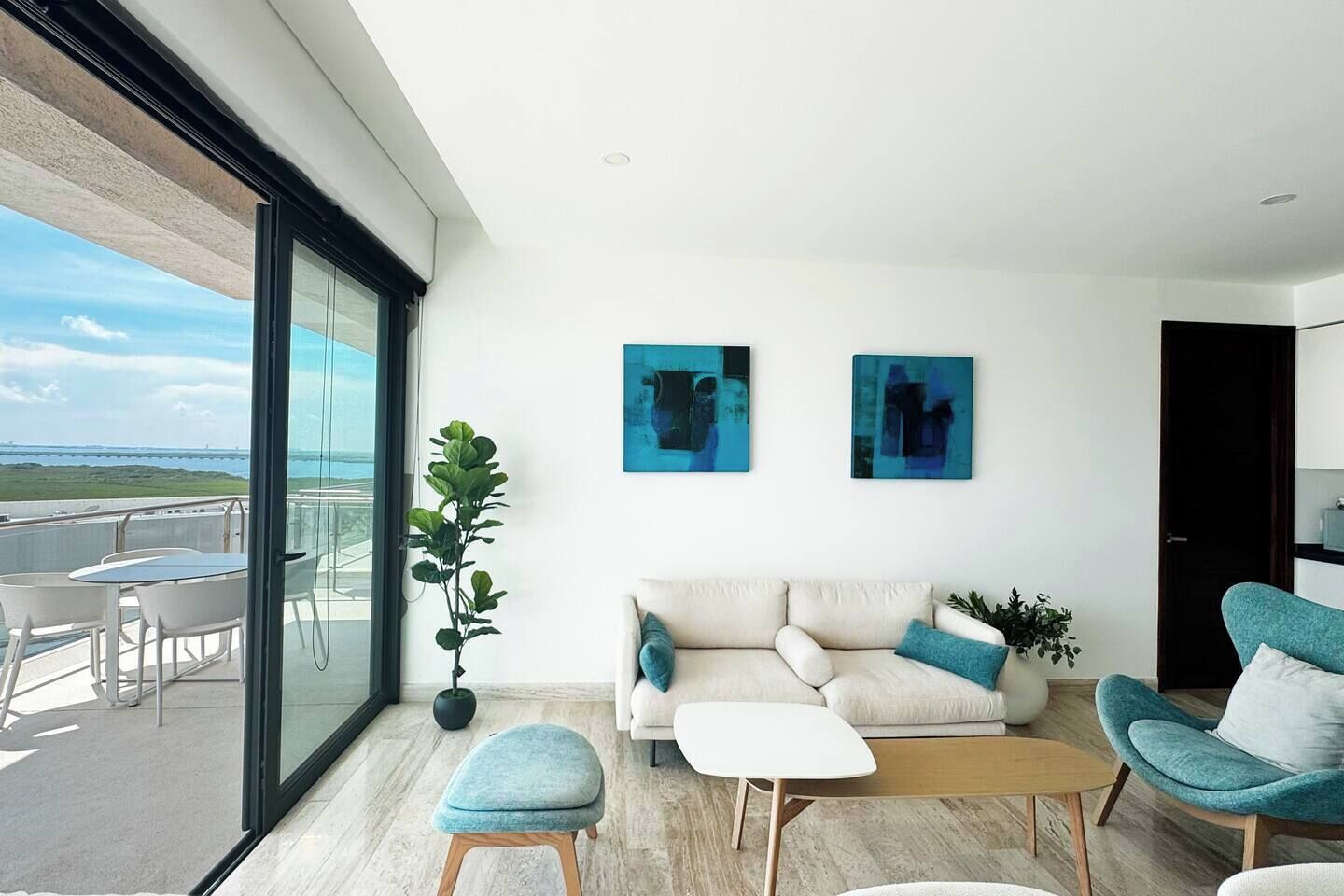 Ein modernes Wohnzimmer mit einer Couch, zwei Sesseln, einem Couchtisch und einem Balkon mit Sitzgelegenheit.