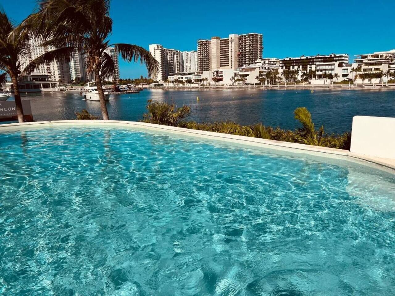 Ein Swimmingpool mit klarem Wasser, umgeben von Palmen und Blick auf eine Marina mit Booten und Gebäuden im Hintergrund.