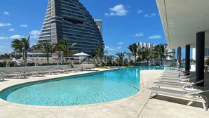 Una piscina con sillas de descanso, palmeras y un edificio moderno al fondo.