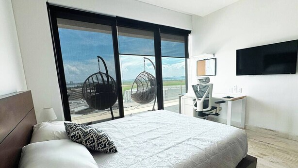 Habitación de hotel con una cama grande, un escritorio con silla, un televisor y vista al aeropuerto.