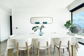 Ein moderner Essbereich mit einem runden Tisch, weißen Stühlen, einer Vase mit Grünpflanzen und einem großen Fenster mit Blick.