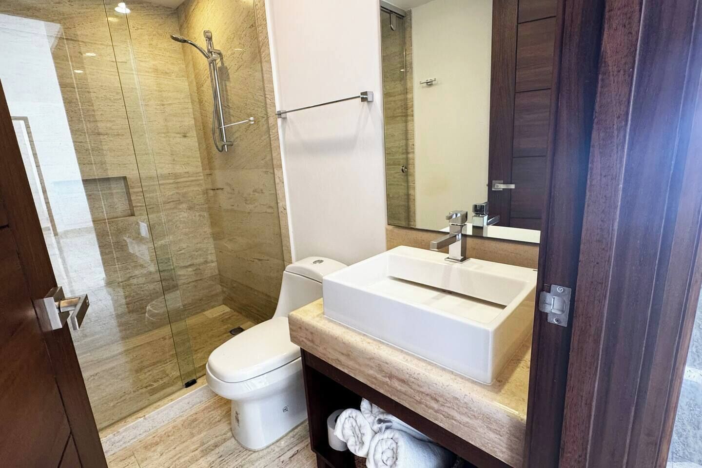 Une salle de bain moderne avec une douche à parois de verre, des toilettes blanches et un grand miroir au-dessus d’un lavabo rectangulaire.