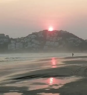A beach with a sunset, a person walking, and buildings in the background. - Villa Brisas del Mar - Acapulco Diamante, Club de Playa (Acapulco de Juarez)