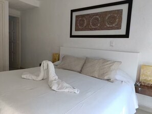 A neatly made bed with a white comforter and two pillows, a framed artwork above the bed, and a door to the left. - Villa Brisas del Mar - Acapulco Diamante, Club de Playa (Acapulco de Juarez)