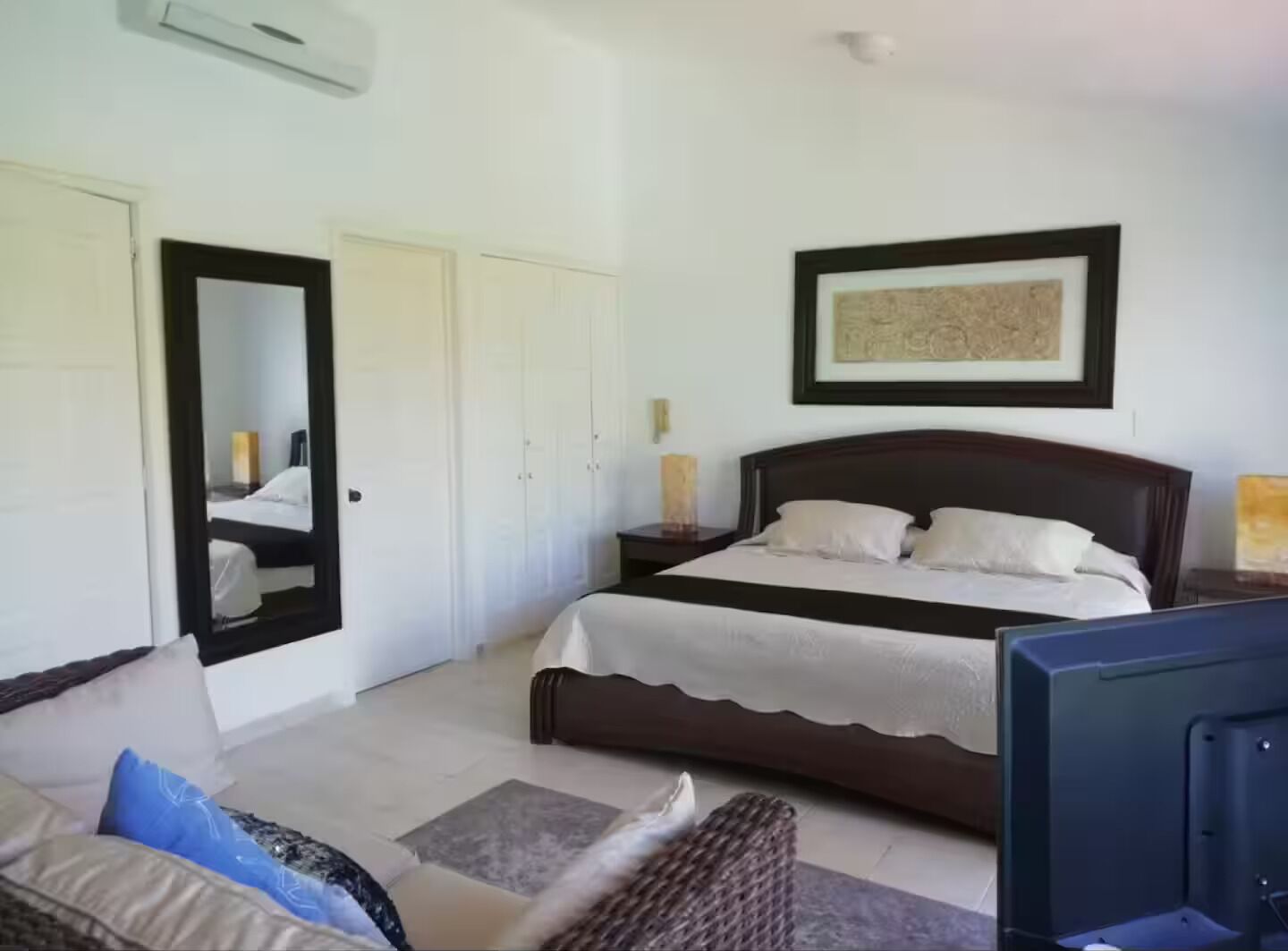 A bedroom with a bed, a mirror, a framed picture, and a television.