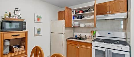 Cocina compacta con armarios de madera, microondas, refrigerador y estufa.