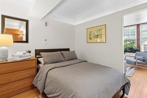 A bedroom with a bed, a dresser, a mirror, a framed picture, and a chair. - Cozy 1-bedroom apartment in charming New Haven with AC (New Haven)
