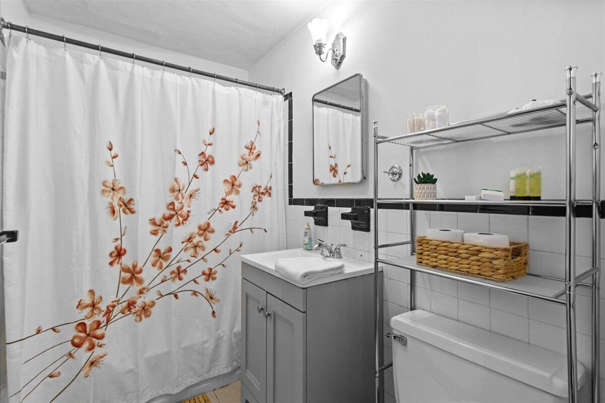 Ein Badezimmer mit Duschvorhang, Waschbecken, Spiegel und Ablagen für Pflegeprodukte.