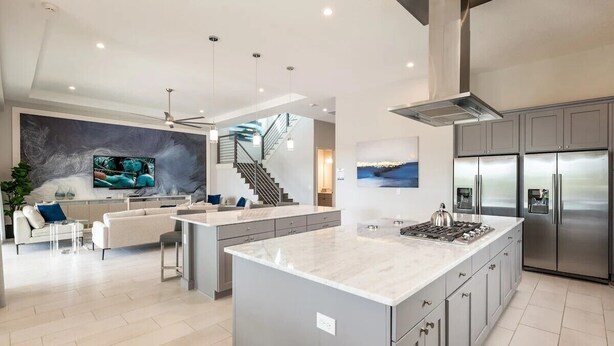 Una cocina moderna con una isla central, electrodomésticos de acero inoxidable y una escalera que conduce a un nivel superior.