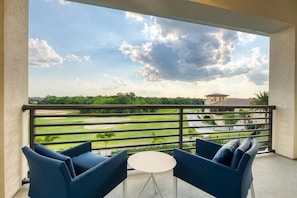 Ein Balkon mit Blick auf einen Golfplatz, zwei blaue Stühle und ein runder Tisch.
