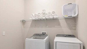 Zona de lavandería con dos lavadoras blancas y un estante con toallas dobladas.
