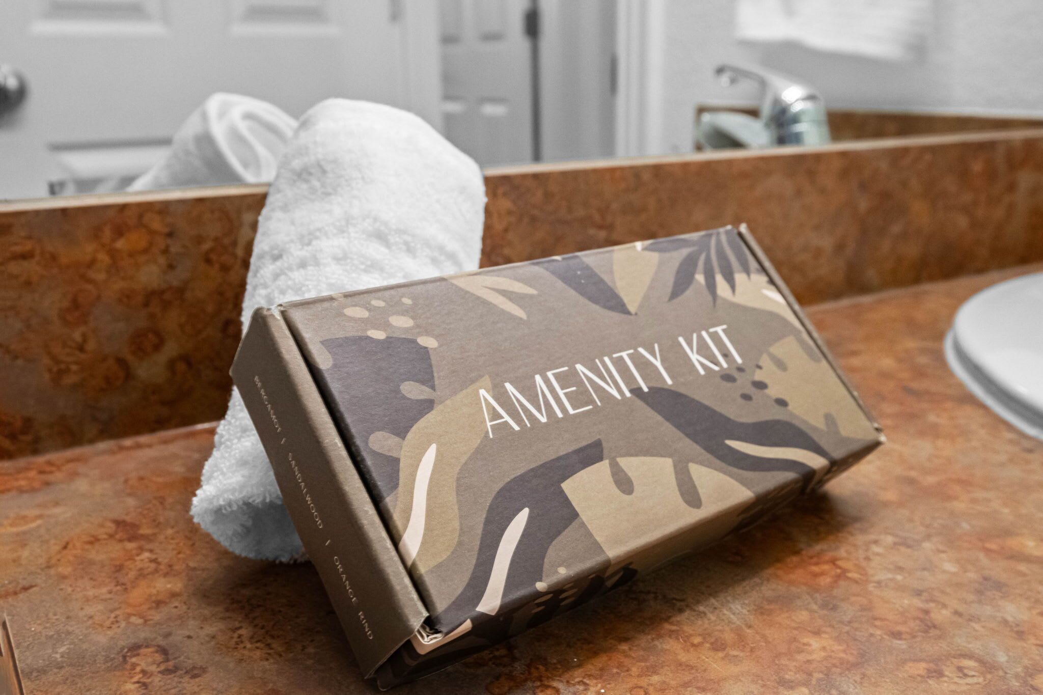 A bathroom with a towel on the counter and a box labeled 'AMENITY KIT' on the sink.