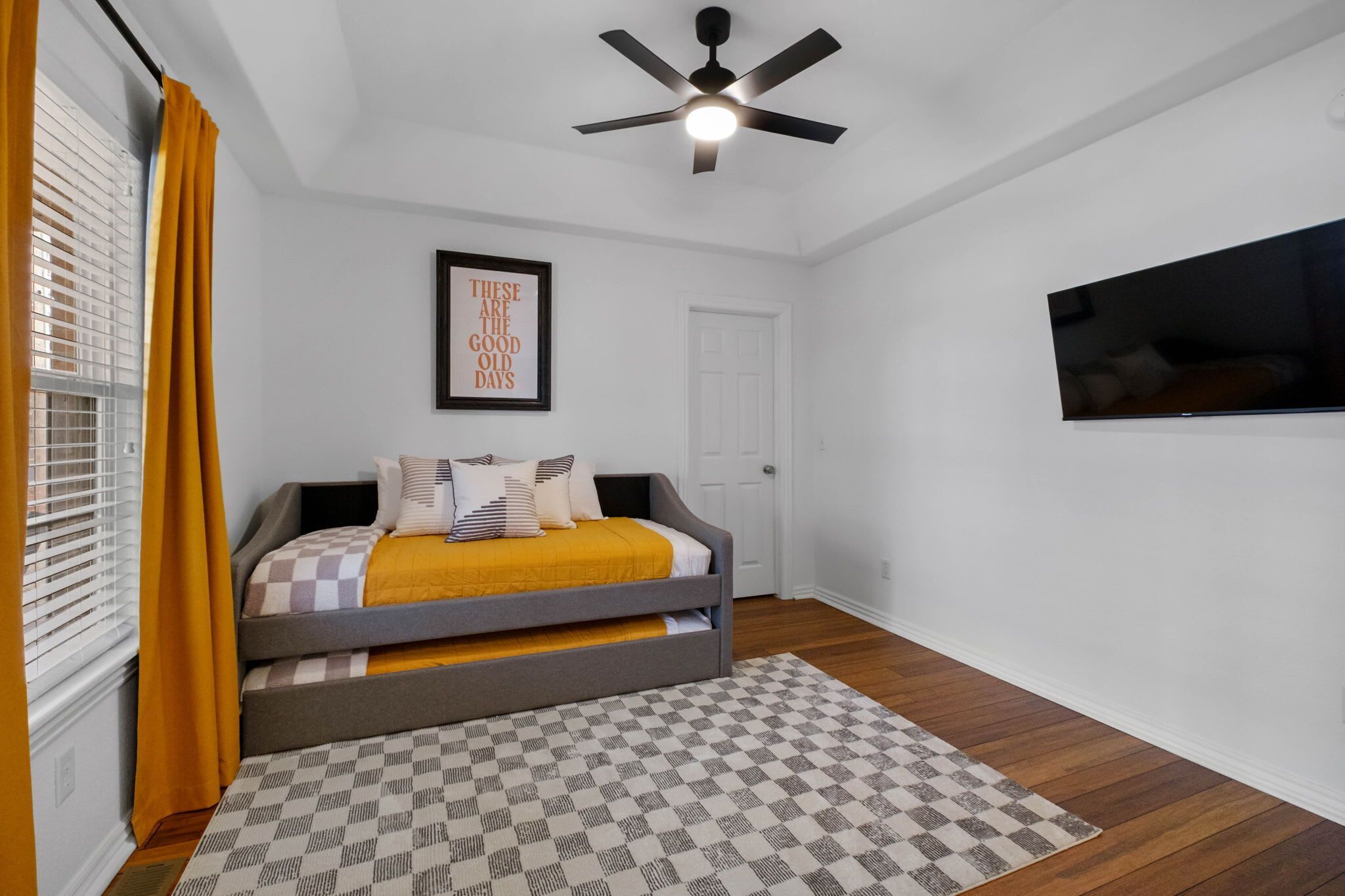 A bedroom with a bed, a ceiling fan, a framed picture on the wall, and a television mounted on the wall.
