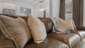 A brown leather sofa with patterned cushions, a hanging light fixture, and a kitchen in the background. - The Witherby Woodland Retreat (Bella Vista)