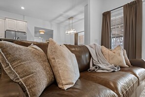 A brown leather sofa with patterned cushions, a hanging light fixture, and a kitchen in the background. - The Witherby Woodland Retreat (Bella Vista)