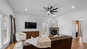 A modern living room with a fireplace, a ceiling fan, and a large flat-screen TV. - The Witherby Woodland Retreat (Bella Vista)