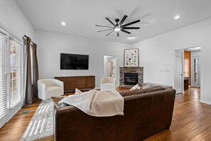 A modern living room with a fireplace, a ceiling fan, and a large flat-screen TV. - The Witherby Woodland Retreat (Bella Vista)