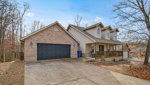 A two-story house with a garage, a covered porch, and a brick exterior. - The Witherby Woodland Retreat (Bella Vista)
