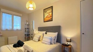 A bedroom with a bed, bedside table, lamp, and a poster on the wall. - L'Ecrin Marin - LA TESTE DE BUCH (LA TESTE DE BUCH)