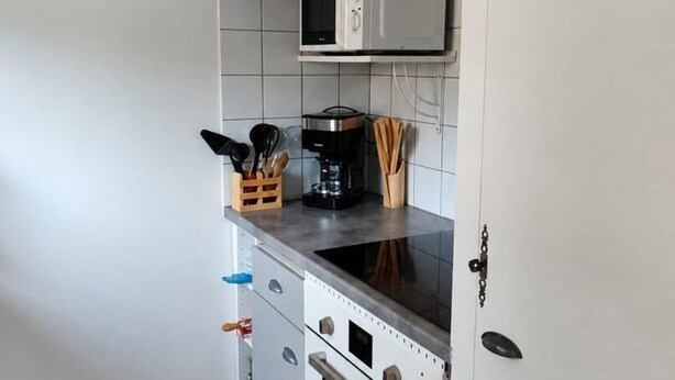 A kitchen with white cabinets, a microwave, a stove, and a clock on the wall. - L'Ecrin Marin - LA TESTE DE BUCH (LA TESTE DE BUCH)