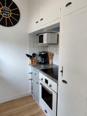 A kitchen with white cabinets, a microwave, a stove, and a clock on the wall. - L'Ecrin Marin - LA TESTE DE BUCH (LA TESTE DE BUCH)