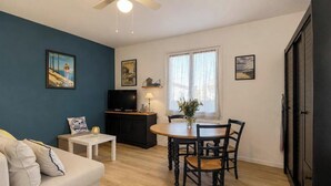 A living room with a sofa, a dining table with chairs, a television, and artwork on the walls. - L'Ecrin Marin - LA TESTE DE BUCH (LA TESTE DE BUCH)