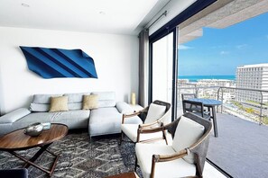 Een moderne hotelkamer met balkon, een bank, twee fauteuils, een kleine tafel en een groot abstract kunstwerk aan de muur.