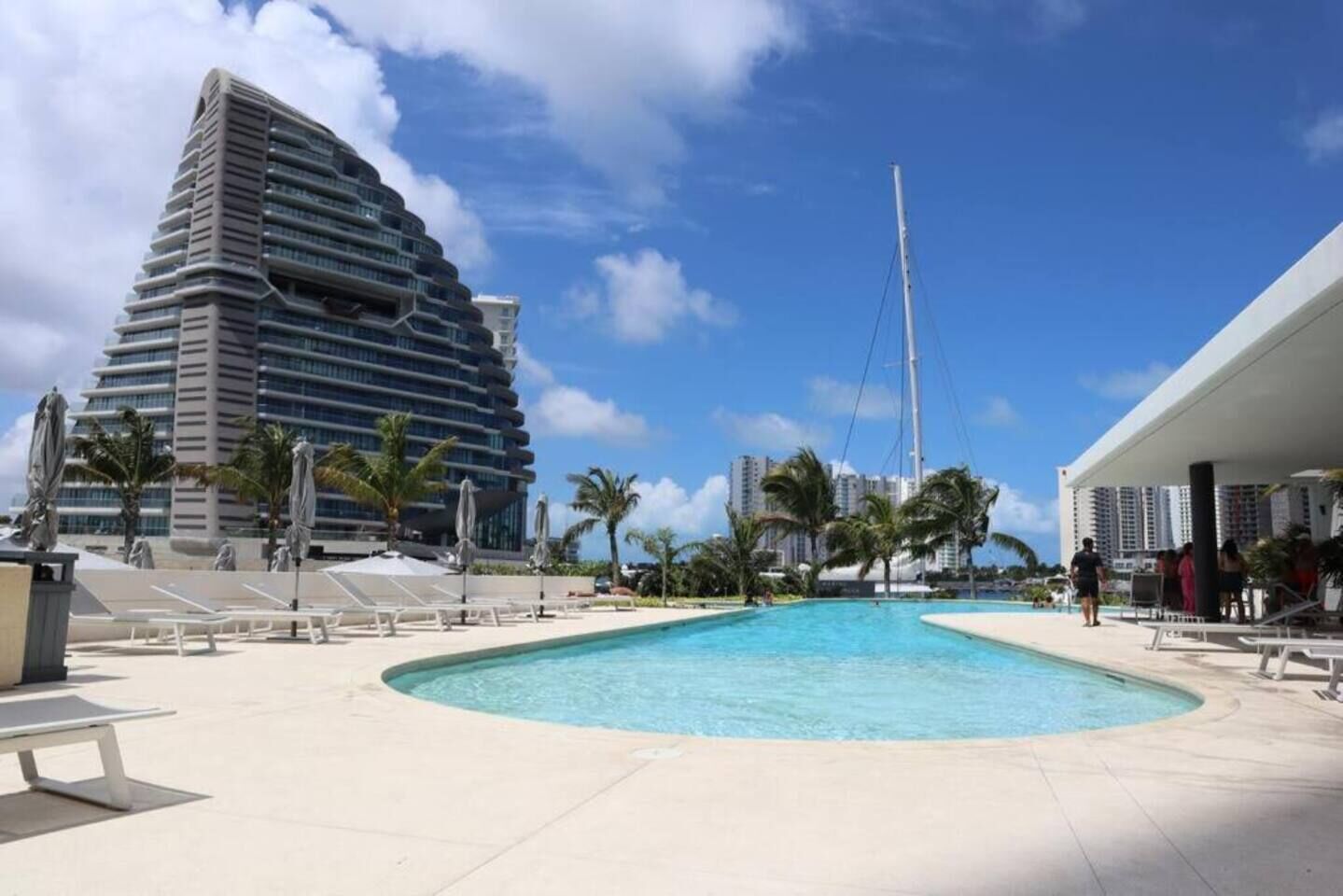 A modern hotel with a pool area, palm trees, and a clear blue sky.