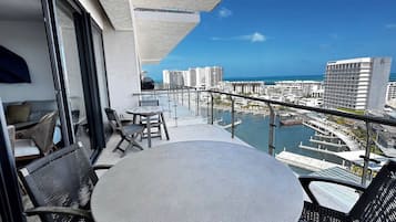A balcony with a round table and chairs, overlooking a marina and high-rise buildings.