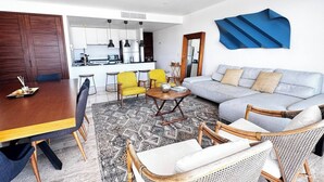Un salon moderne avec un canapé, des fauteuils, une table à manger et un coin cuisine à l’arrière-plan.