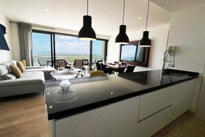 Een moderne keuken met een groot eiland, hanglampen en uitzicht op de stad door grote ramen.