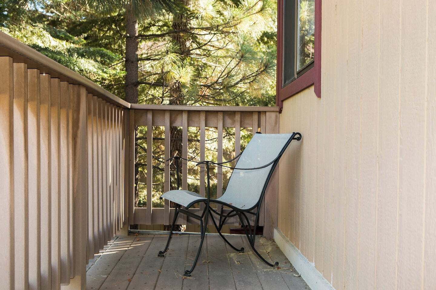 Eine Holzterrasse mit einem Metallstuhl und einem Tisch, umgeben von Bäumen.