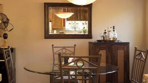 A dining area with a round glass table, metal chairs, a wooden cabinet with bottles, and a mirror on the wall. - Ultimate Mountain Retreat! (South Lake Tahoe)