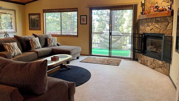 A living room with a stone fireplace, a sofa set, and a view through glass doors to an outdoor area. - Ultimate Mountain Retreat! (South Lake Tahoe)
