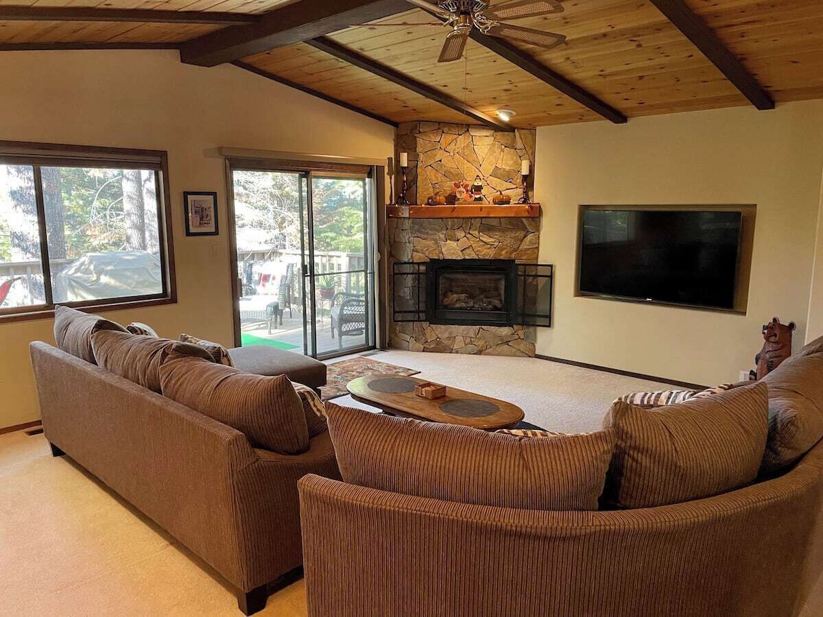 A living room with a stone fireplace, a flat-screen TV, and a ceiling fan.