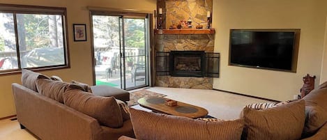 A living room with a stone fireplace, a flat-screen TV, and a ceiling fan.