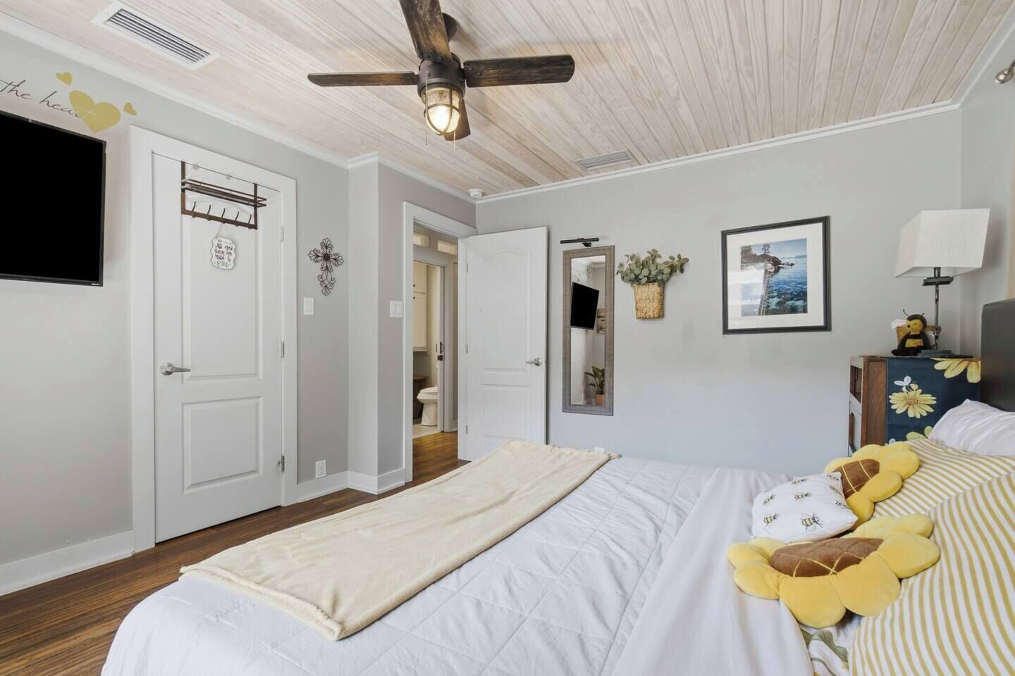 A bedroom with a bed, a ceiling fan, a television mounted on the wall, and a bedside table with a lamp.