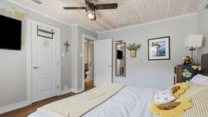 A bedroom with a bed, a ceiling fan, a television mounted on the wall, and a bedside table with a lamp.
