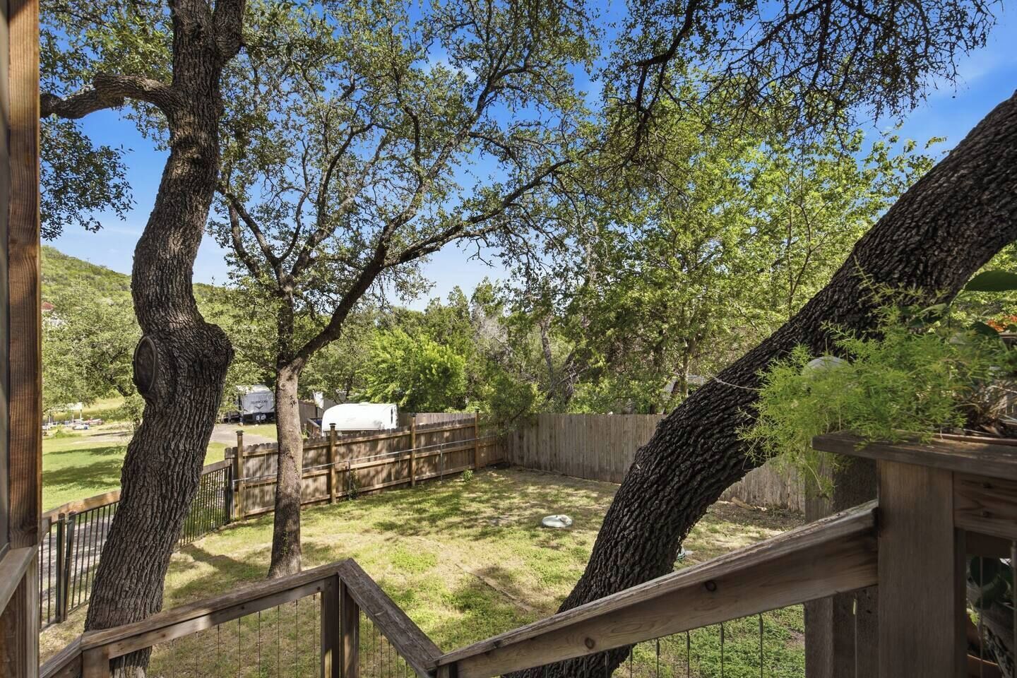 A fenced backyard with trees, a wooden deck, and a white storage tank.