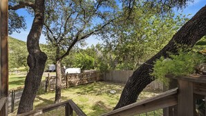 A fenced backyard with trees, a wooden deck, and a white storage tank.