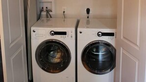 A laundry room with two front-loading washing machines, a self-service sign, and a shelf with various items. - Lake Travis Lakefront Cabin with Cowboy Pool (Leander)