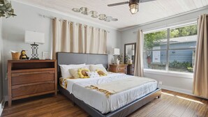 A bedroom with a bed, wooden dresser, bedside tables, a ceiling fan, and a window with curtains. - Lake Travis Lakefront Cabin with Cowboy Pool (Leander)