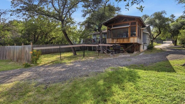 A wooden cabin with a deck, surrounded by a wooden fence and trees. - Lake Travis Lakefront Cabin with Cowboy Pool (Leander)