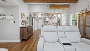 A modern interior with a sofa, wooden beams, and a kitchen in the background.