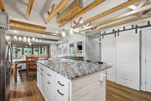Una cocina amplia con una isla de mármol, vigas de madera, luces colgantes y una puerta corredera.