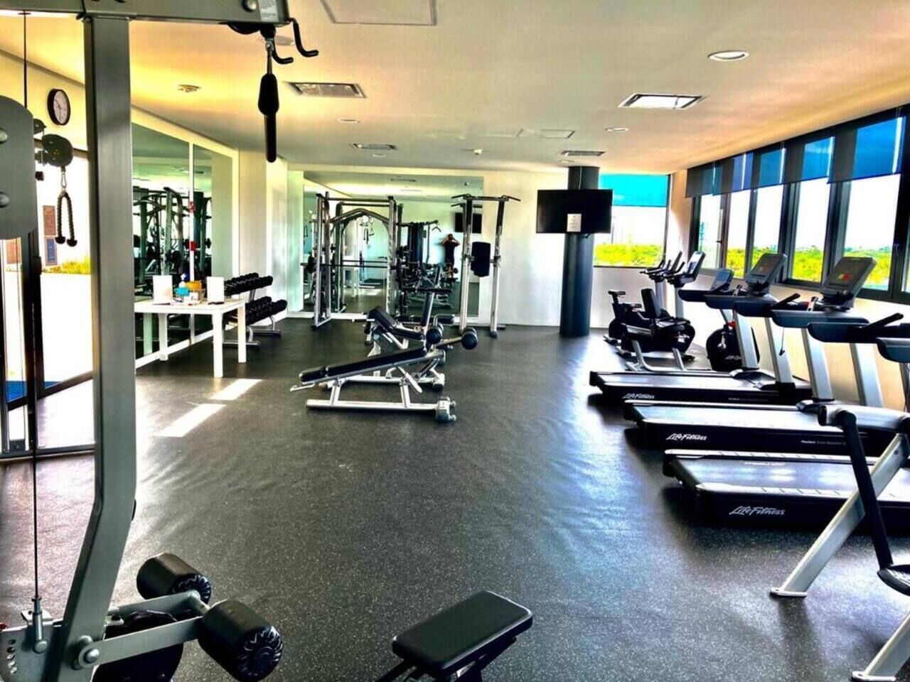Ein Fitnessstudio mit Laufbändern, Kraftgeräten und einer Spiegelwand.