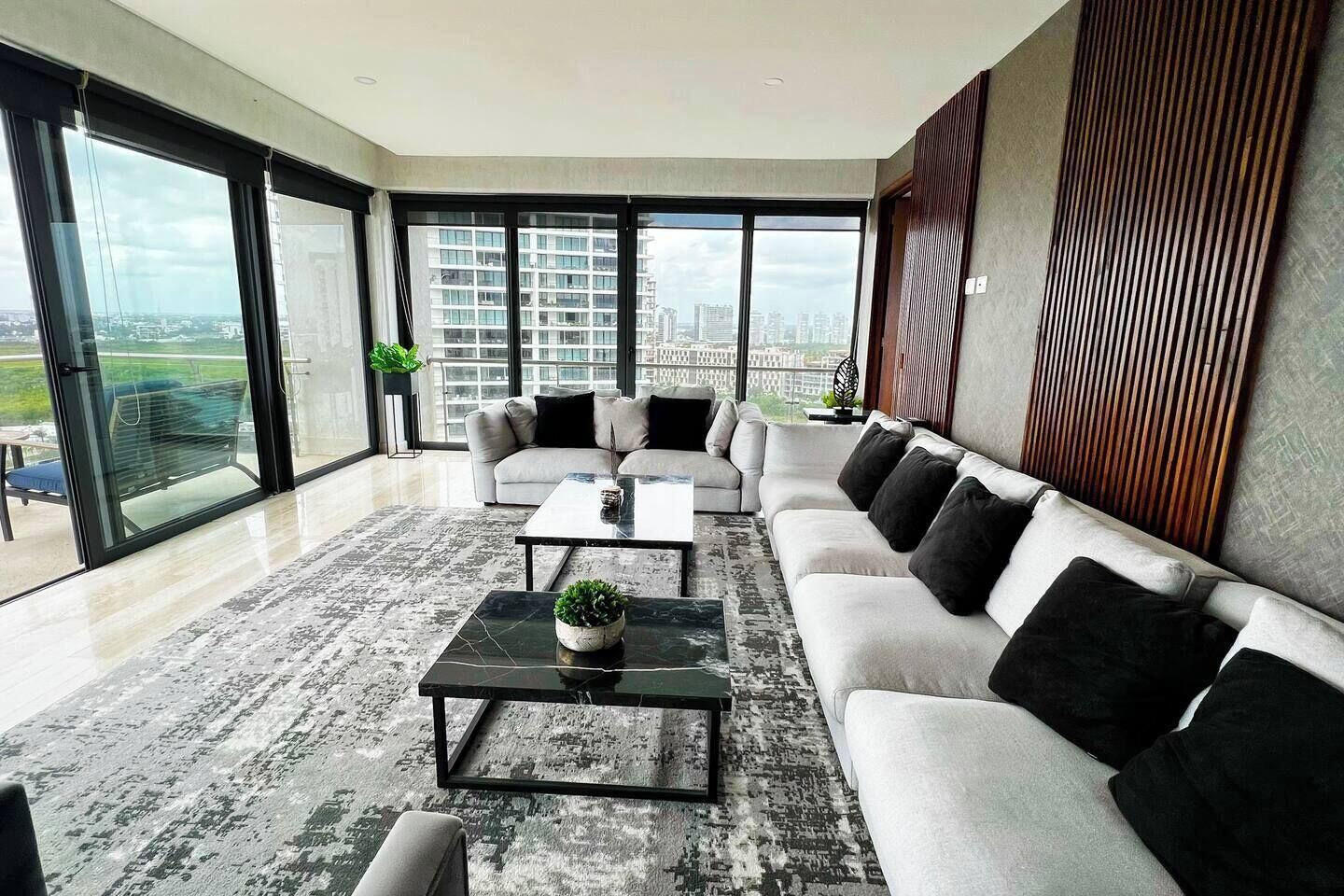 A modern living room with a large sofa, a coffee table, and a view of a cityscape through large windows.
