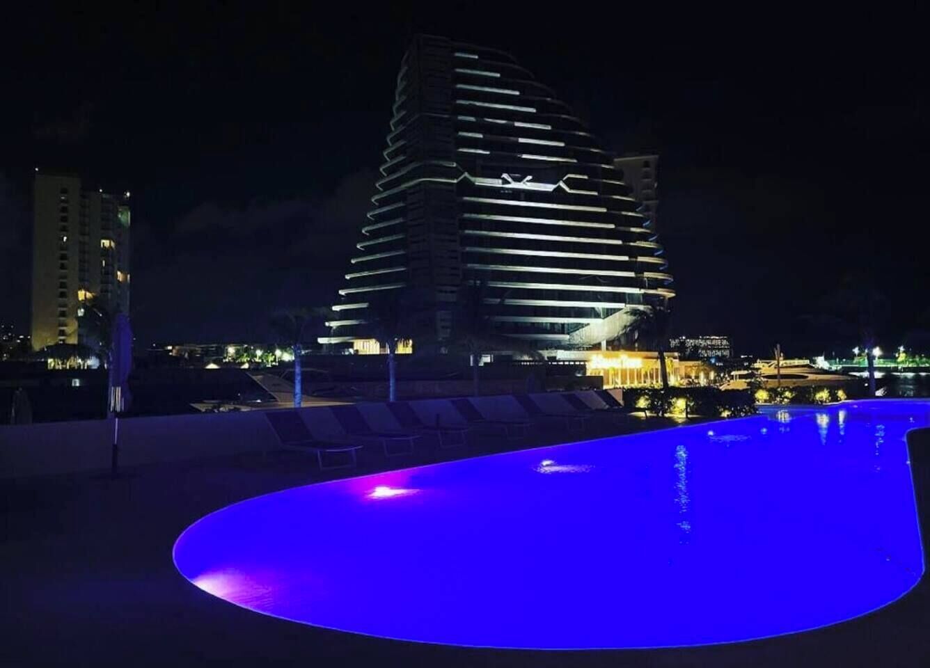 Une scène nocturne mettant en scène un bâtiment moderne et une piscine éclairée de lumière bleue.