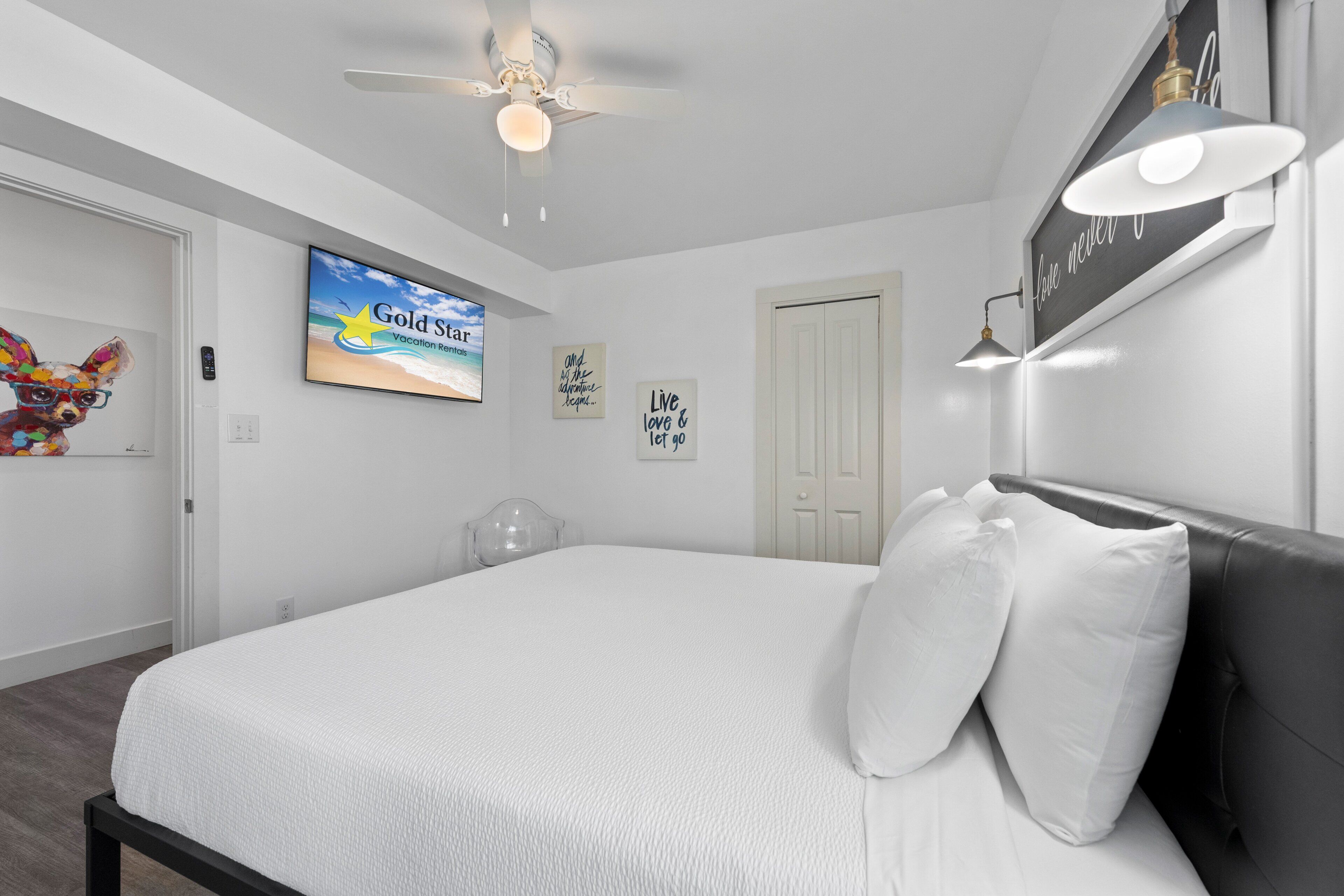 Un dormitorio con cama, ventilador de techo, televisor y decoración en la pared.