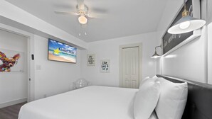 Quarto com cama, ventilador de teto, televisão e obras de arte nas paredes.